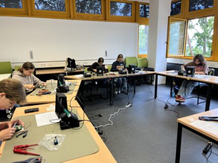 Schülerinnen sitzen an Tischen und bauen gemeinsam einen sogenannten „ewigen Kreisel“.